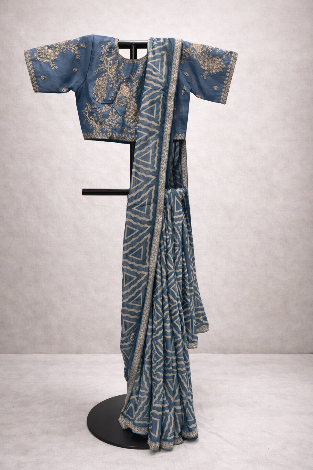 Blue saree with intricate patterns on a stand against a plain background